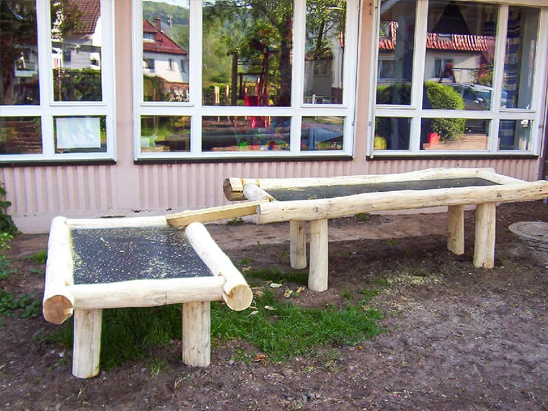 Zwei Matschtische aus Robinienholz im Hof eines Kindergartens